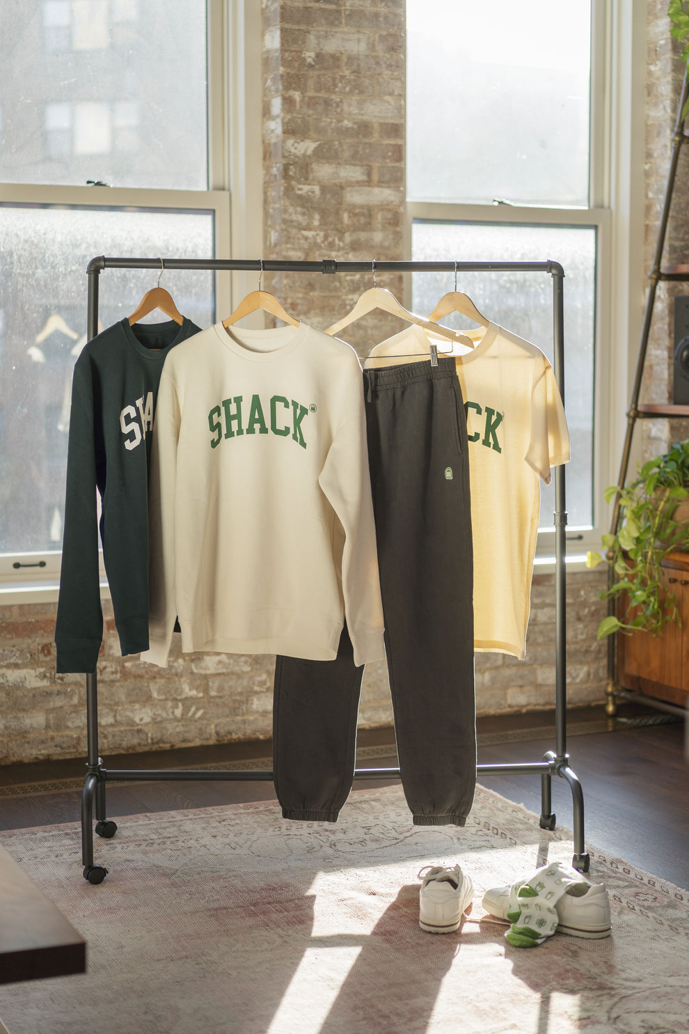Forest green sweatshirt, cream-colored sweatshirt, black sweatpants, and cream-colored t-shirt on coat hangers