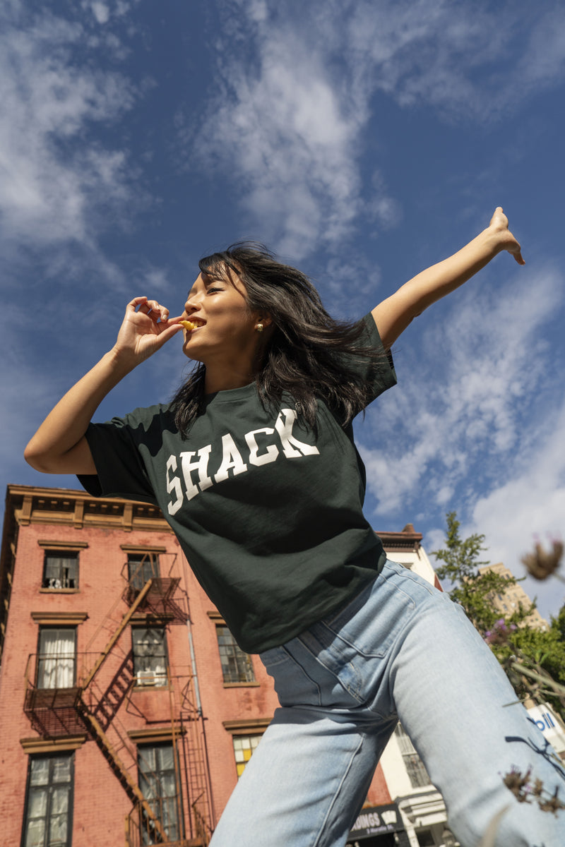 Girl outside wearing forest green Shake Shack tee and enjoying Shake Shack fries